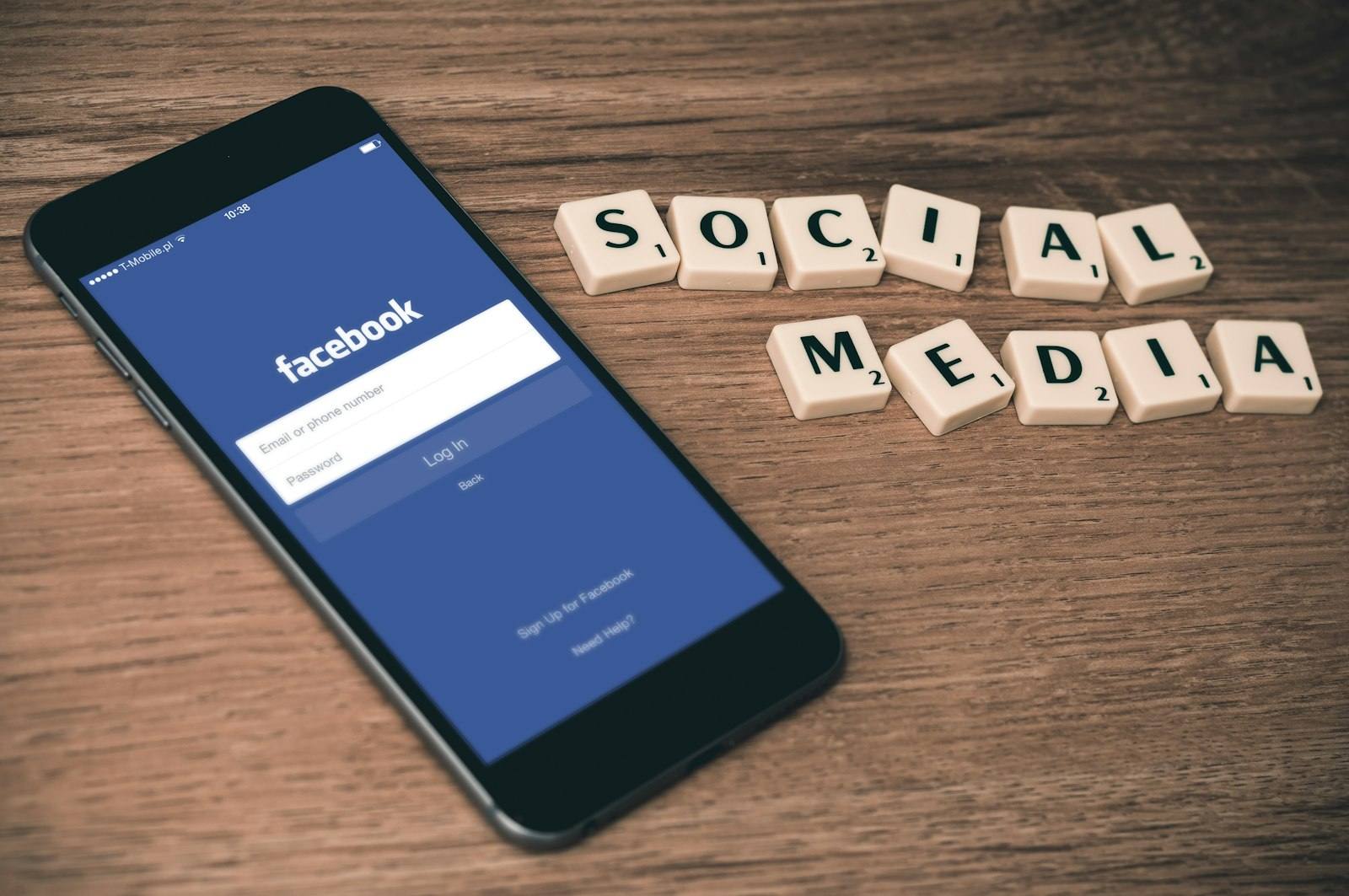 A smartphone showing a social network login screen beside wooden tiles spelling social media