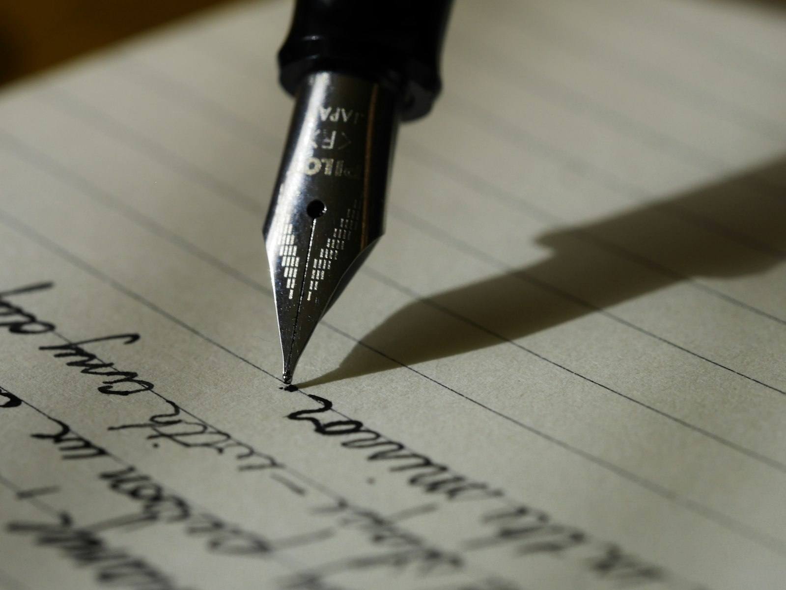 A fountain pen nib writing cursive script on lined paper