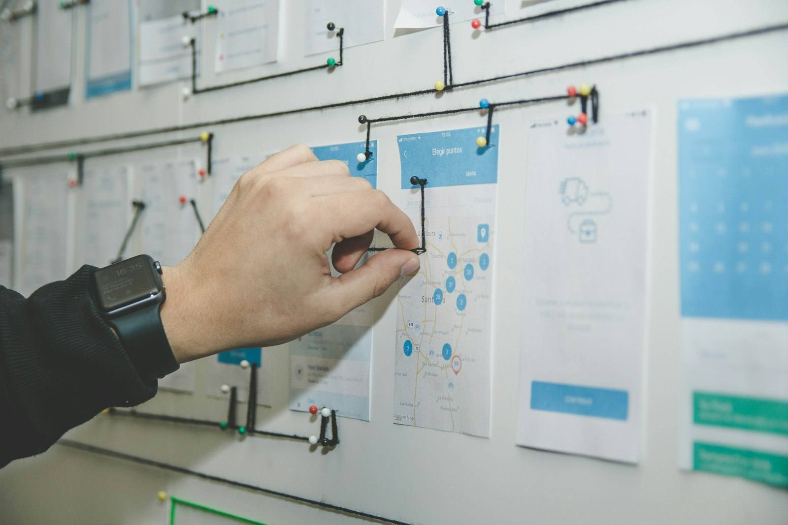 A person arranging interface wireframe sketches pinned to a whiteboard
