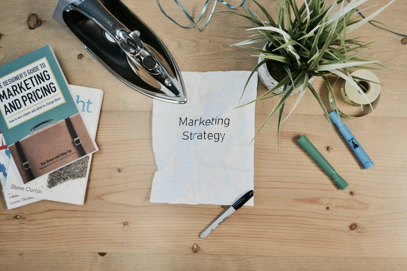 A flat lay of a marketing strategy notepad, a book and pens on a wooden desk