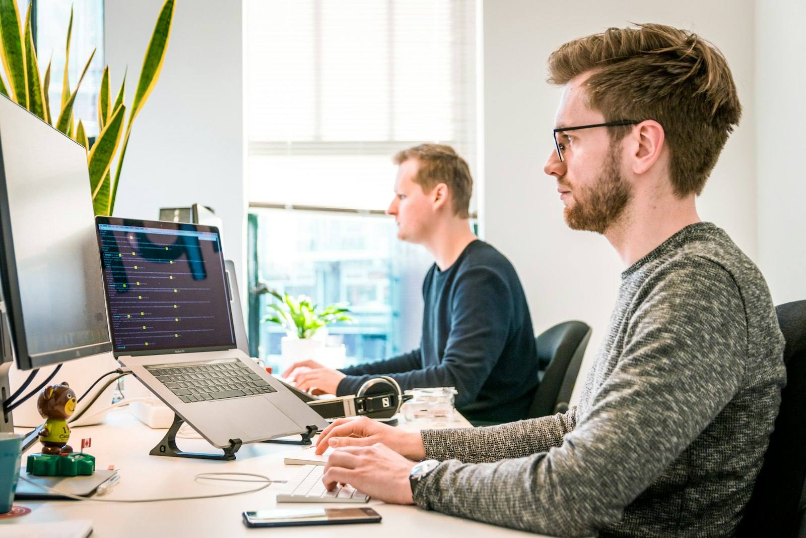 Two colleagues working side by side at monitors in a bright office