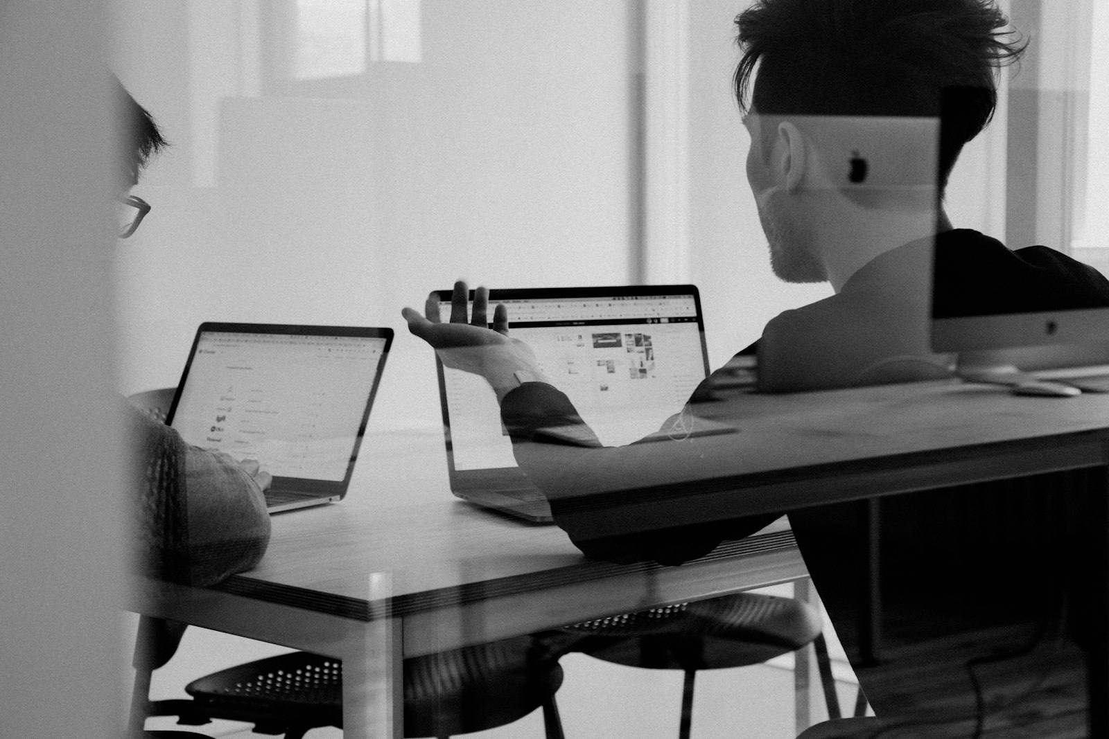 A black and white view of people working at a desk seen through a glass wall