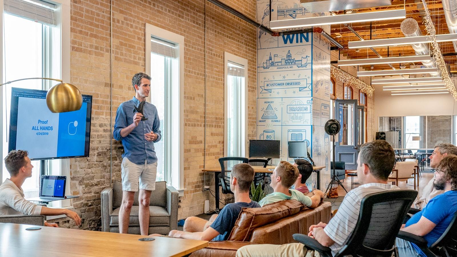 A speaker addressing a seated audience in a brick-walled open office