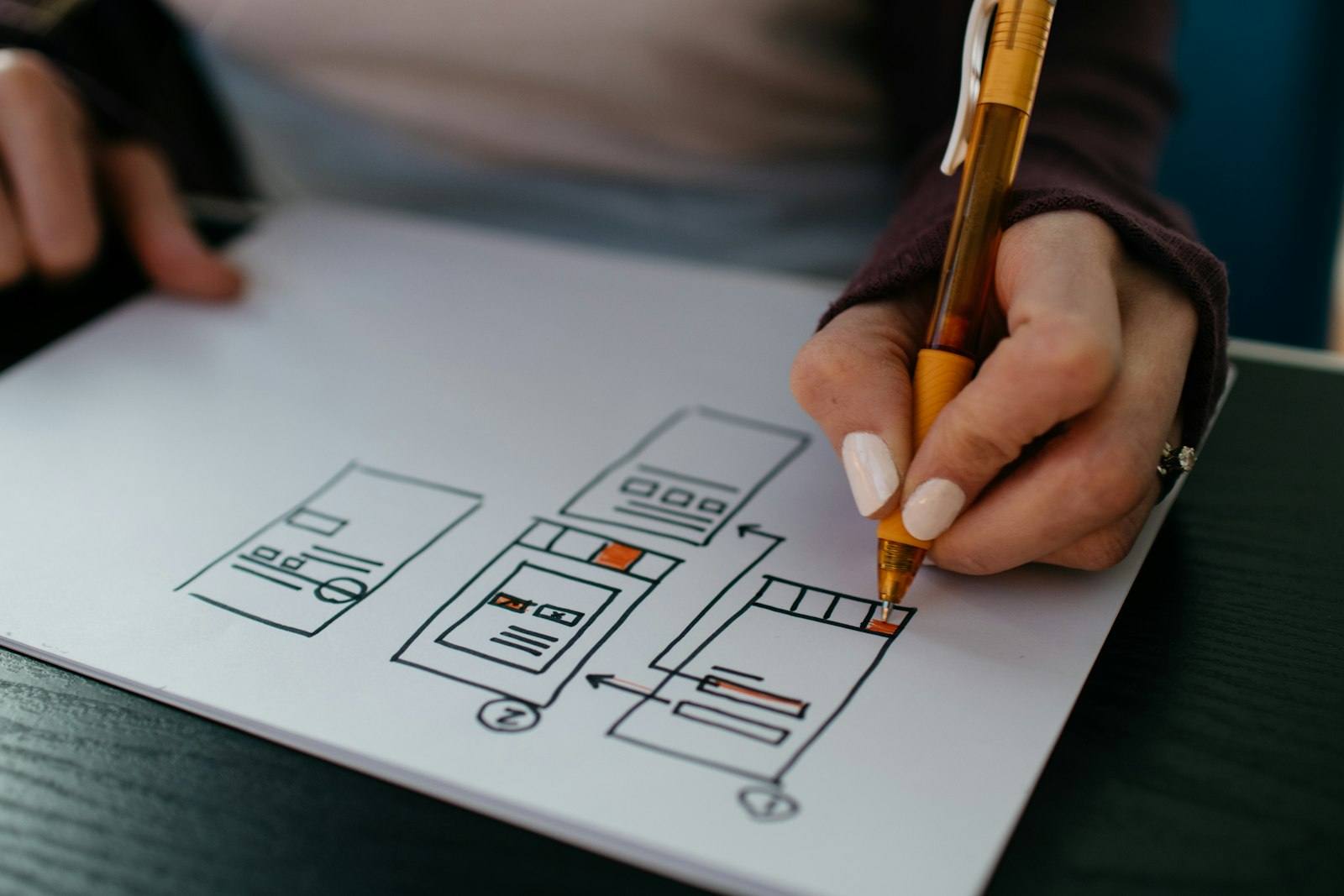 A hand sketching a web page wireframe layout with a pen